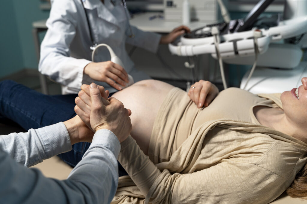 Pregnant woman receiving an ultrasound, with her partner's supportive hands, representing compassionate prenatal care at Mythri Fertility Centre.